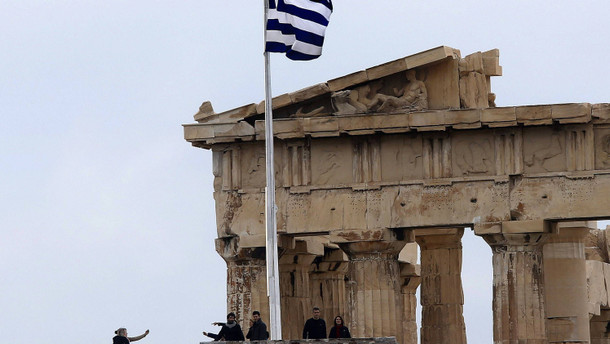 Tourists stand next to the temple of Parthenon atop the ancient site of the Athens Acropolis in a cold and windy day