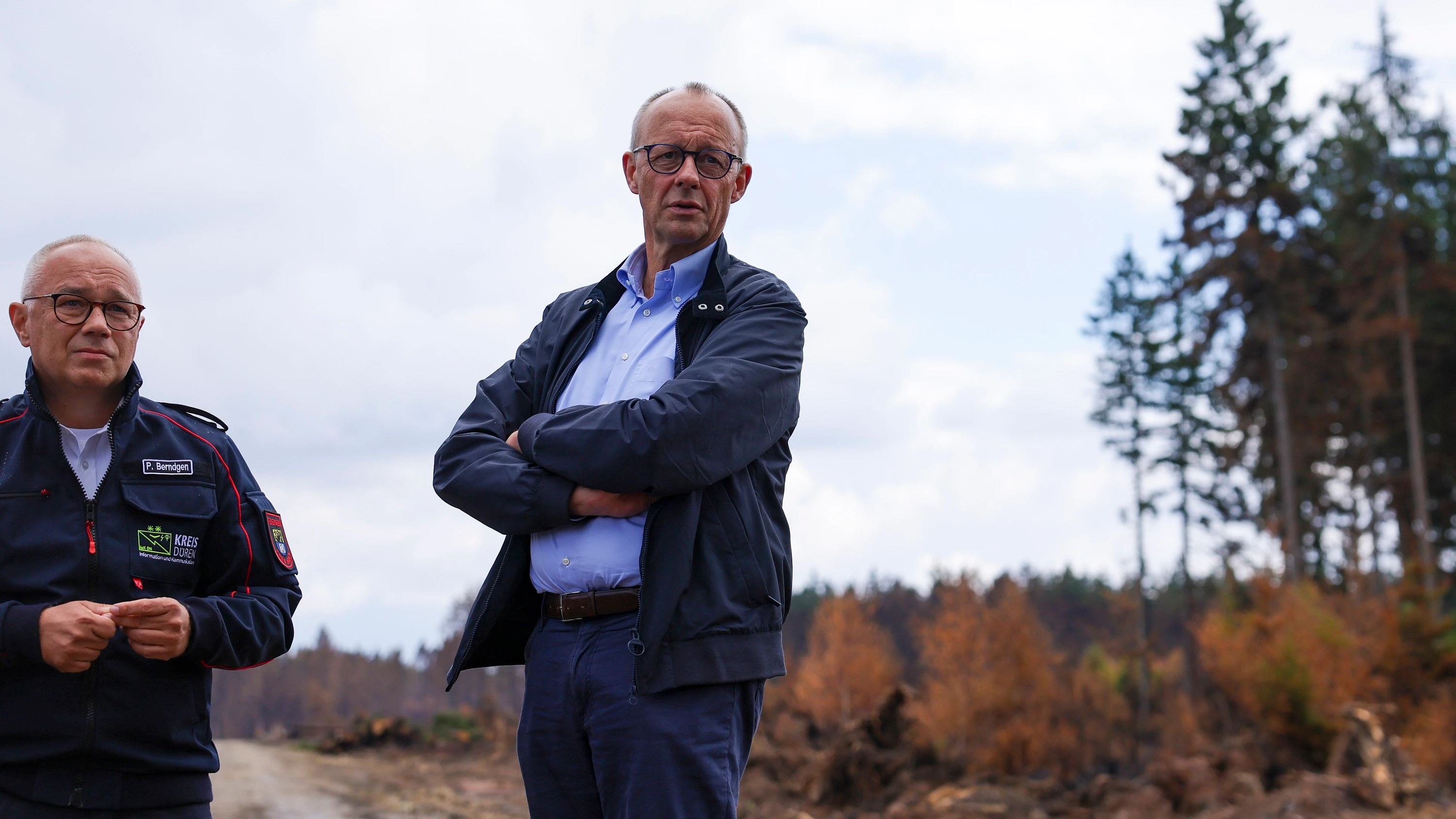 Nach dem Brand: Kanzler Friedrich Merz am Samstag im Hürtgenwald, links ein Sprecher der Feuerwehr - EPA