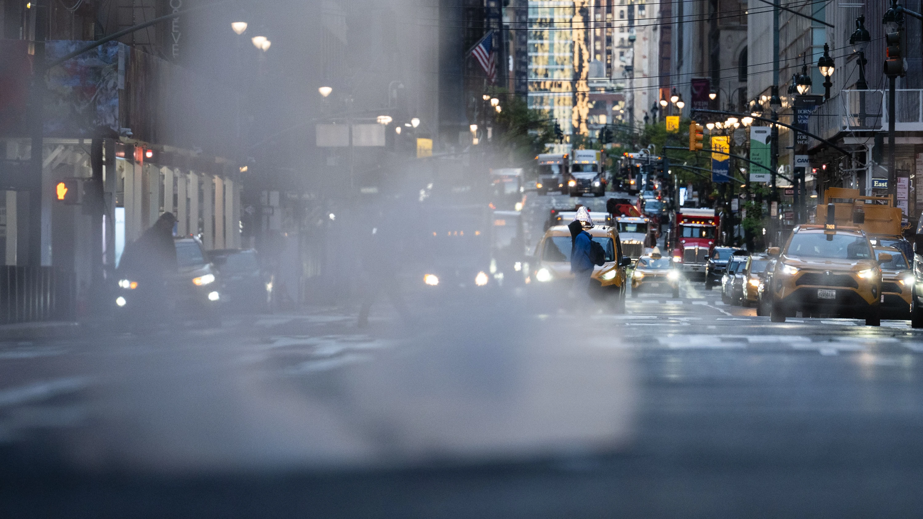 Verkehr ist am frühen Morgen im Stadtteil Manhattan unterwegs, aus einem Gully steigt Dampf auf. - dpa