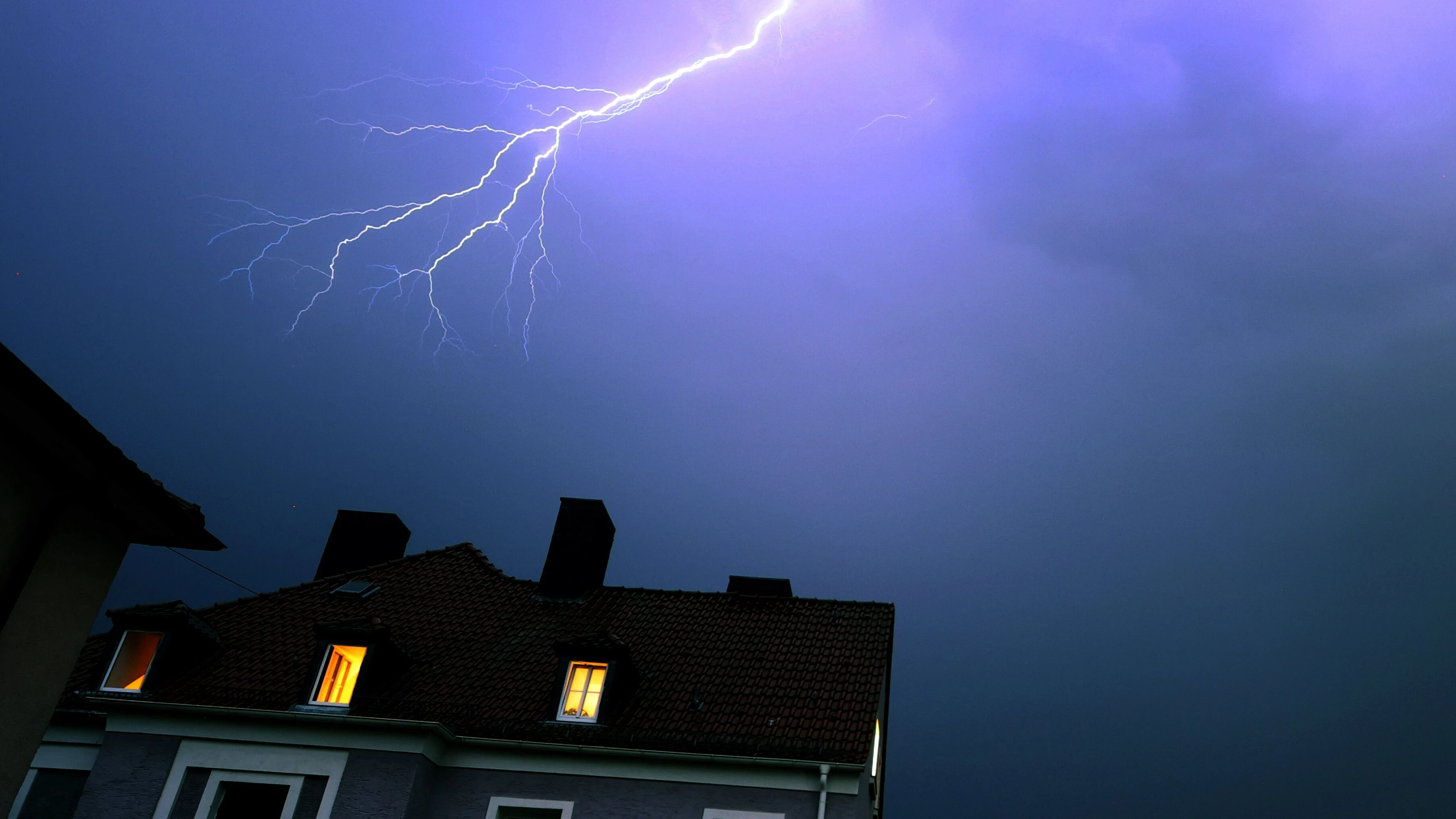 Blitze entladen sich während eines Gewitters über einem Wohnhaus. - dpa