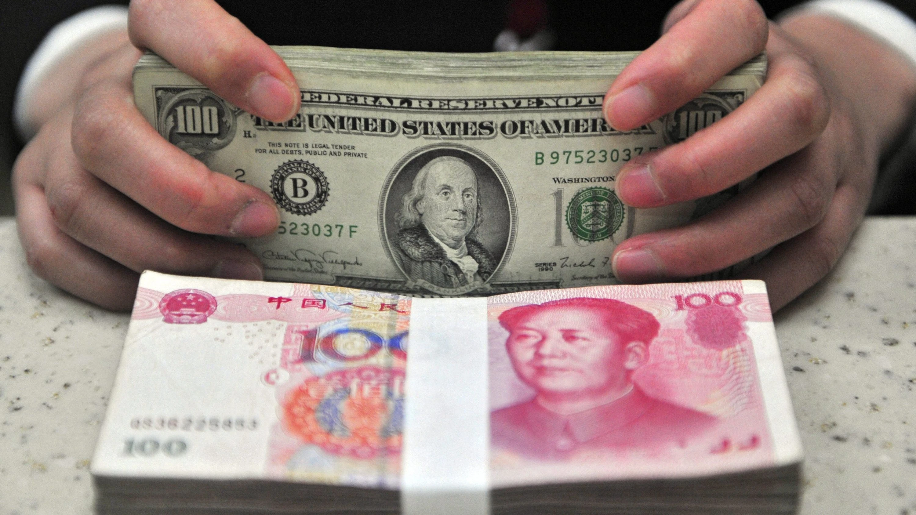 Wer wiegt schwerer – Benjamin Franklin oder Mao Zedong? Ein Kassierer in China zählt Dollar und chinesische Renminbi. - dpa