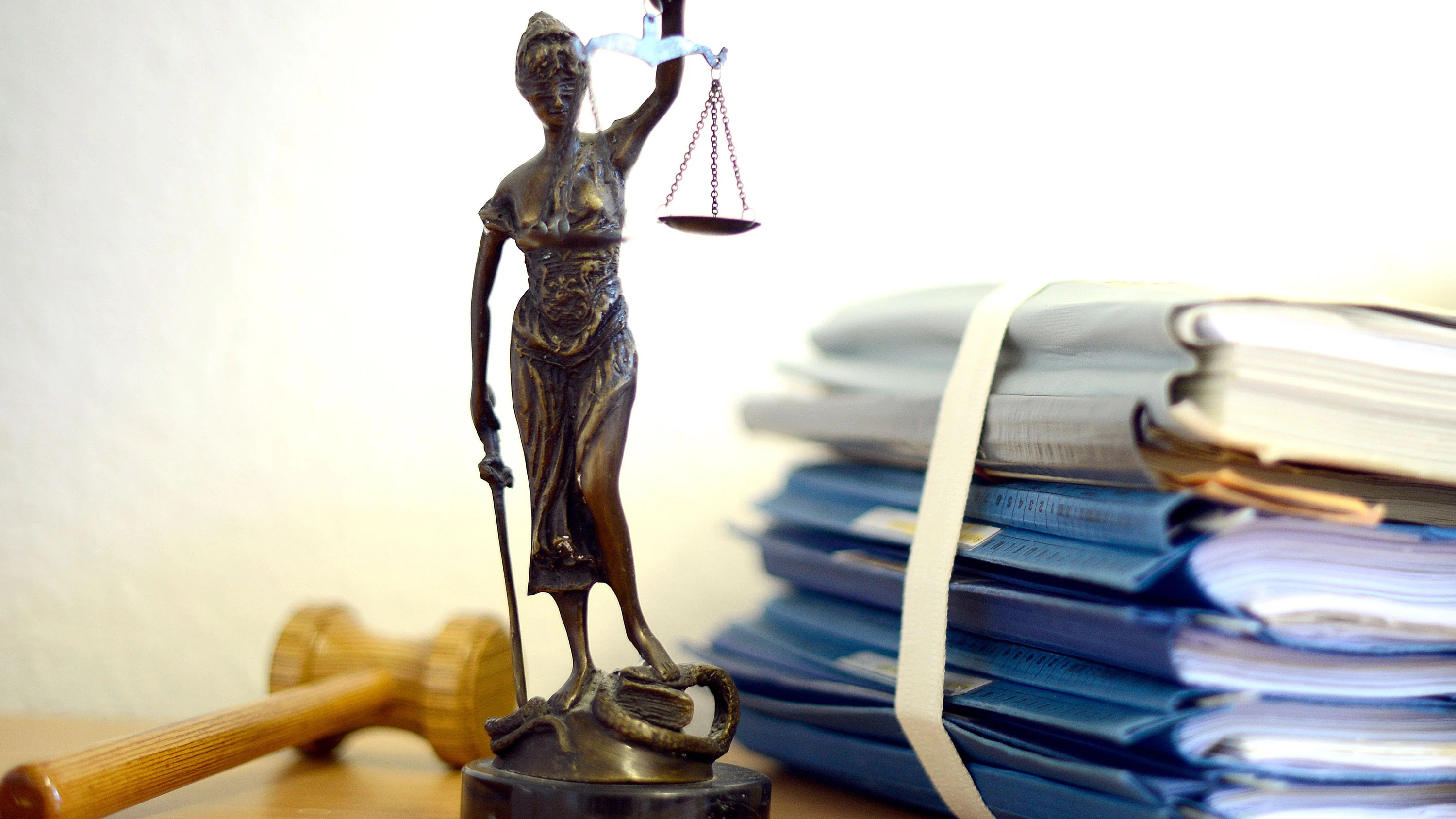 Eine Statue der Justitia steht neben einem Holzhammer und einem Aktenstapel. (Symbolbild) - dpa