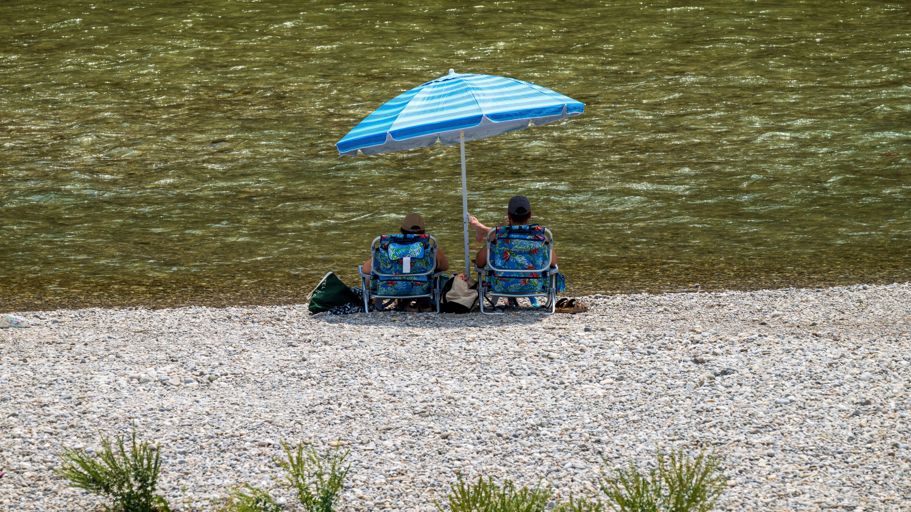 Ein Pärchen sitzt auf einer Kiesbank am Ufer der Isar (Archivbild) - dpa