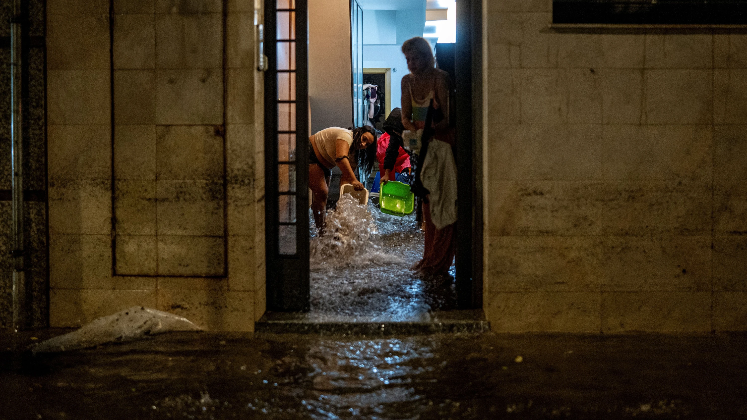 In L'Hospitalet de Llobregat nahe Barcelona: Menschen versuchen, das Wasser aus einem überfluteten Hauseingang zu schöpfen. - dpa