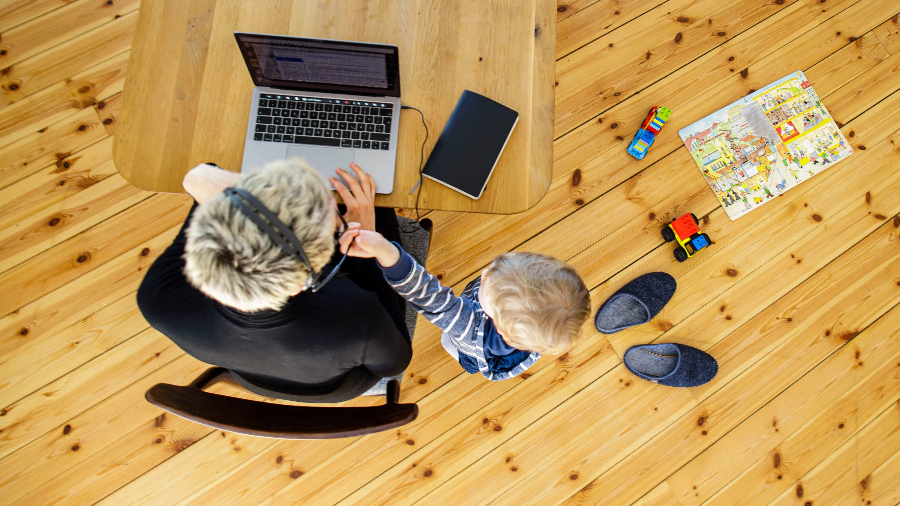 Eine Frau sitzt zu Hause am Schreibtisch und arbeitet, neben ihr spielt ein Kind. - Picture Alliance