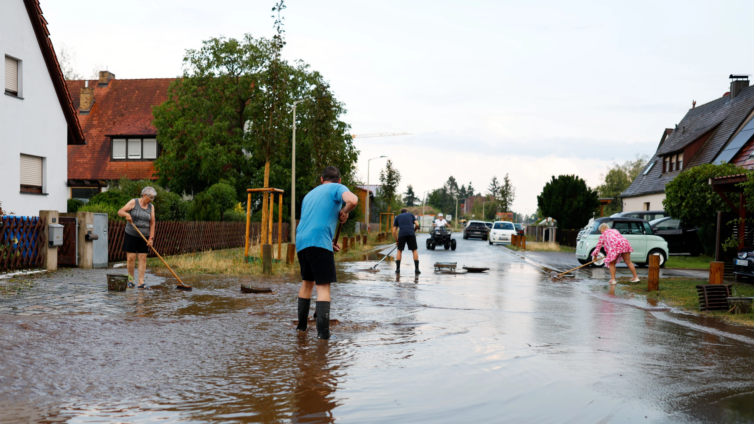 Anwohner schieben nach einem Gewitter in Erlangen das Wasser von der Straße. - dpa