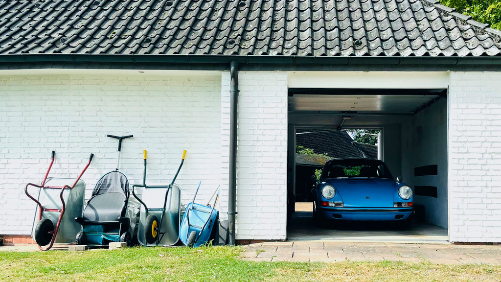Sportwagen in der Garage, Schubkarren vor der Hauswand
