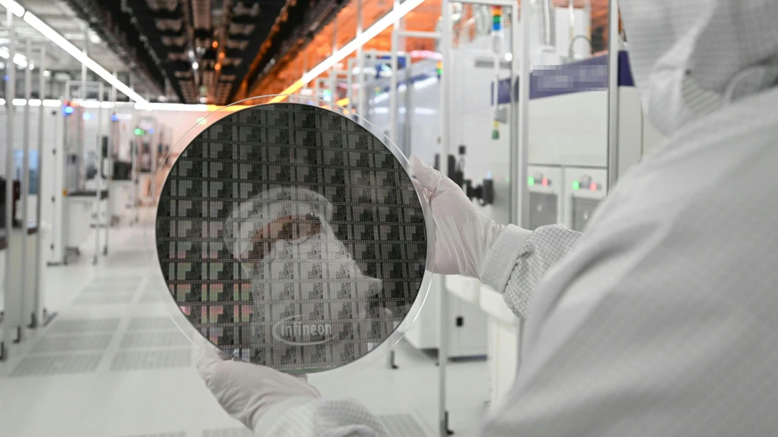 Ein Infineon-Mitarbeiter spiegelt sich in einer Wafer-Scheibe, aus der Chips gefertigt werden, im vollautomatisierten Reinraum der Chipfabrik in Österreich.