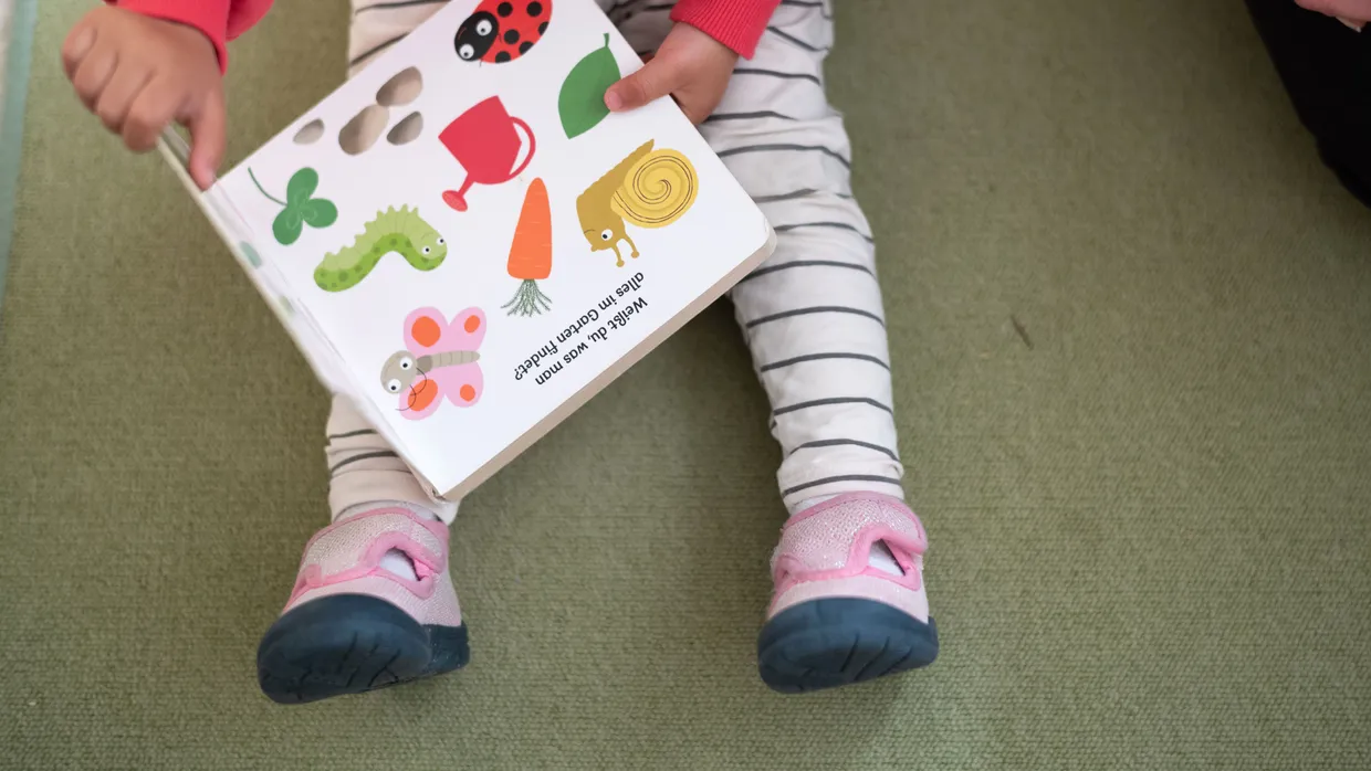 Gut aufgehoben: Ein Kleinkind sitzt mit Bilderbuch in einer Kita.
