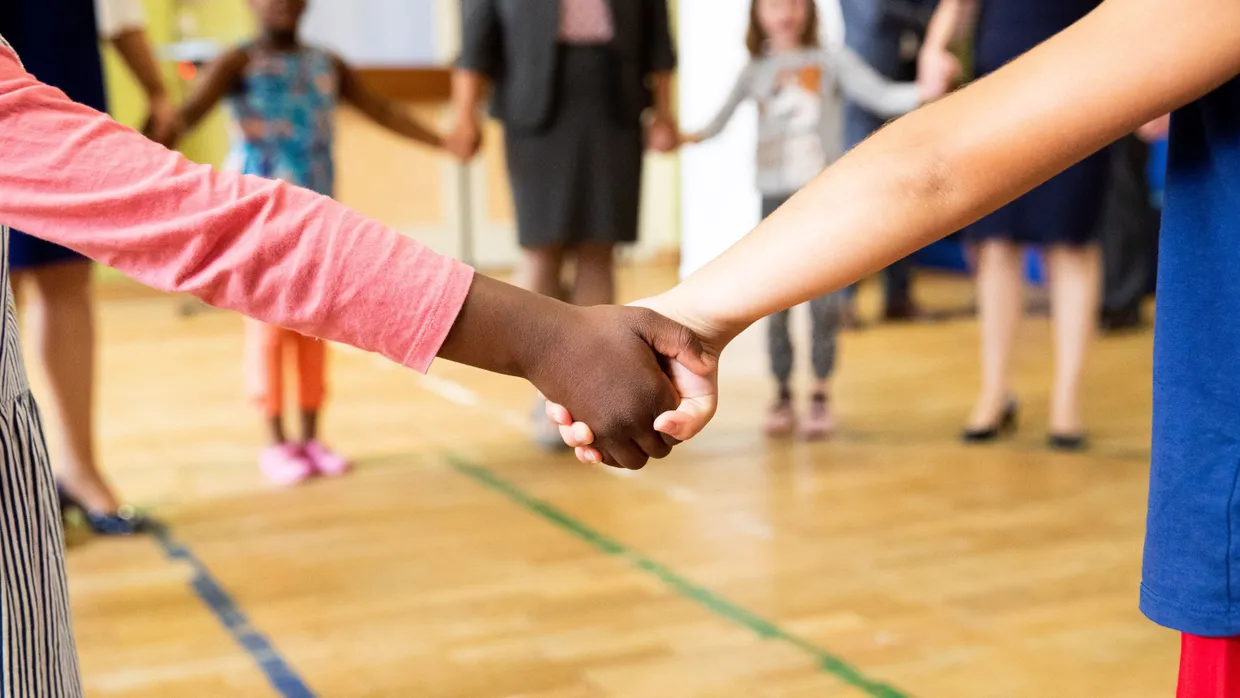 Hand in Hand tanzen Kinder und Erzieherinnen bei einem Bewegungsspiel in der Turnhalle einer Kita