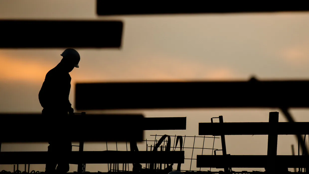 Die Silhouette eines Arbeiters zeichnet sich in einer Aufnahme aus dem August 2021 auf einer Baustelle in Hannover vor dem Morgenhimmel ab
