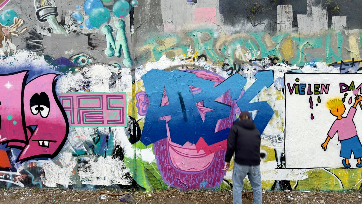 Graffiti-Sprüher bemalt eine Mauer in Berlin-Kreuzberg.