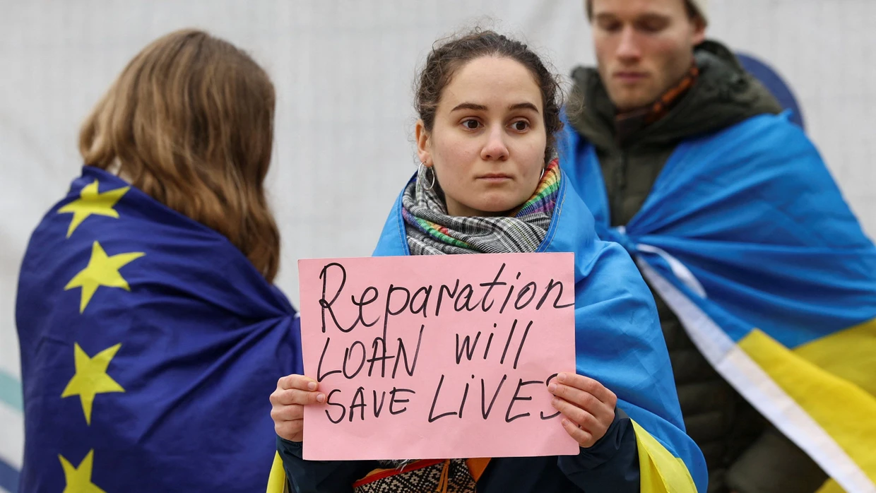 „Das Reparationsdarlehen wird Leben retten“ steht auf einem Schild, das eine Frau hält. Sie demonstriert mit anderen am 17. Dezember vor dem Gebäude der EU-Kommission in Brüssel.