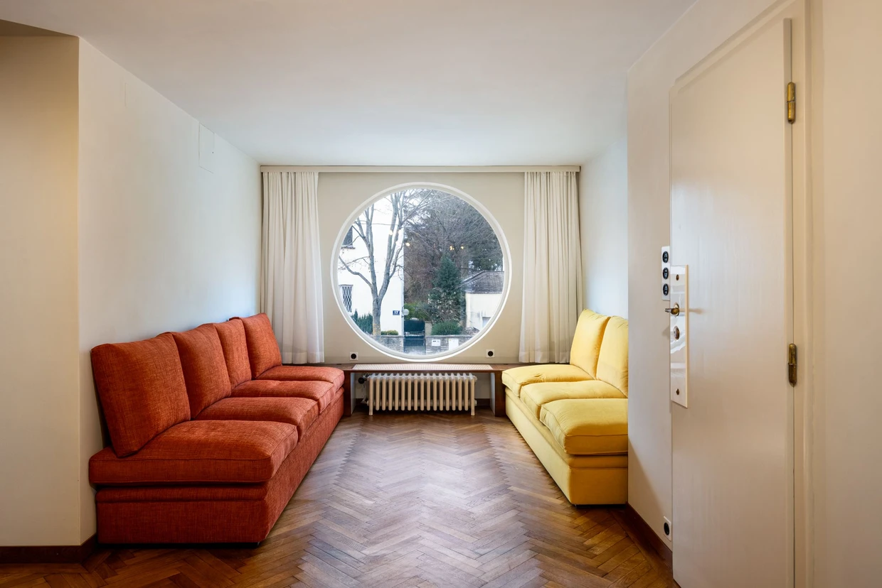 Markantes Rundfenster Richtung Straßenseite, die Sofas sind zeitgenössisch, folgen aber dem Farbentwurf der Architekten