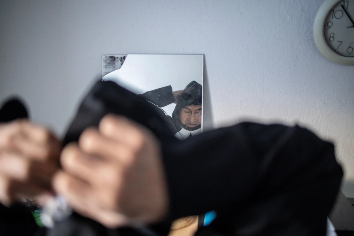 Der Dorfkatechat Ringsted zieht vor einem Spiegel sein liturgisches Gewand an.