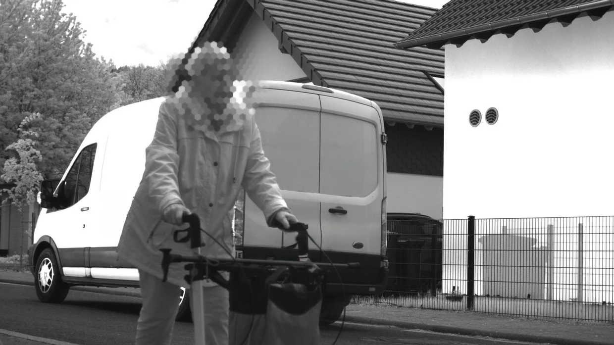 Ein Kastenwagen fährt zu schnell, als eine Frau mit Rollator durch das Bild läuft.