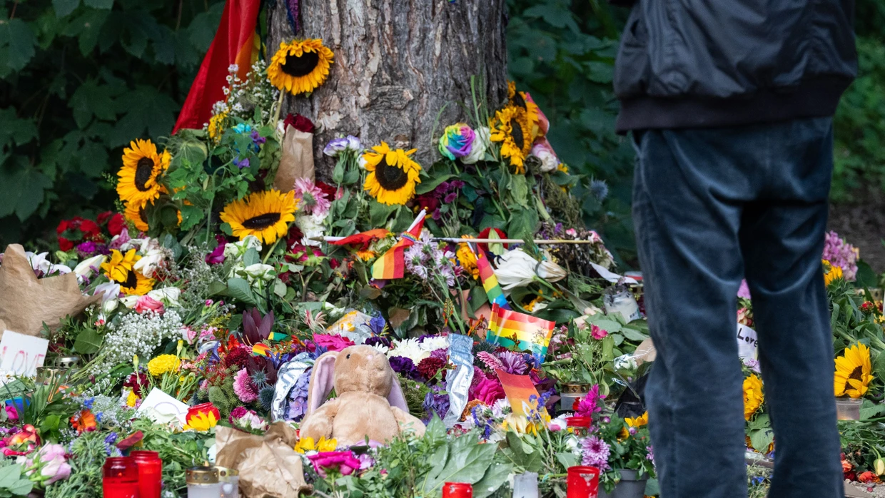 Trauernde stehen im Tiergarten in Berlin an einem Baum, an dem Blumen zum Gedenken an die Opfer des Anschlags auf den CSD niedergelegt wurden.
