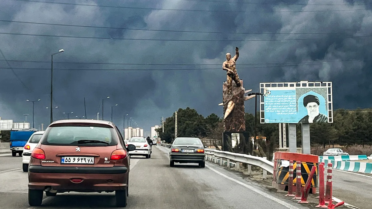 Fahrzeuge in Teheran am 8. März 2026 bewegen sich auf einer Autobahn an einem Kriegerdenkmal und einer Plakatwand vorbei, die Irans verstorbenen Obersten Führer Ayatollah Ali Khamenei darstellt.