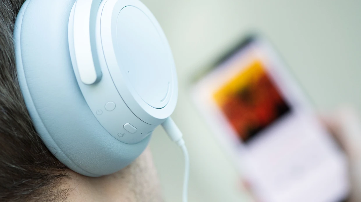 Ein junger Mann hört mit Kopfhörern Musik von seinem Smartphone. (Symbolbild)