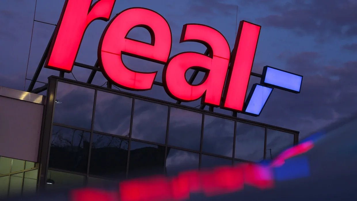 Das Logo leuchtet am Morgen auf dem Dach eines Real Supermarktes.