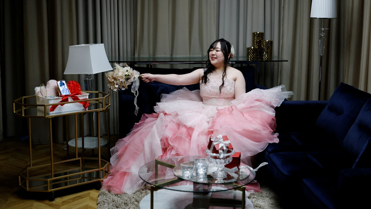 Yurina Noguchi winkt nach ihrer symbolischen Hochzeit mit einem Blumenstrauß dem Bild ihres virtuellen Partners Klaus auf dem Smartphone zu. „Ich habe Klaus nicht gewählt, um der Realität zu entfliehen, sondern als jemanden, der mich im Leben unterstützt“, sagt sie.