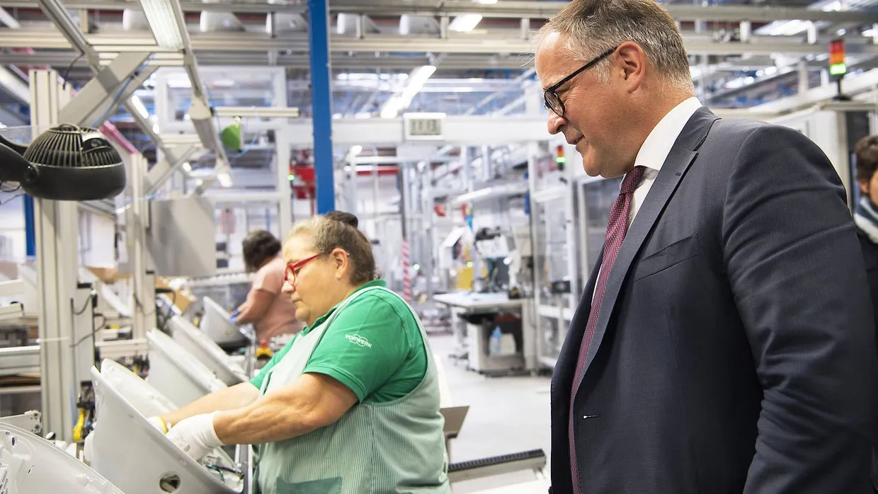 Was die Frau in der Montagehalle wohl denkt? EZB-Direktoriumsmitglied Benoit Coeuré zu Besuch in einer Vorwerkfabrik in Frankreich.