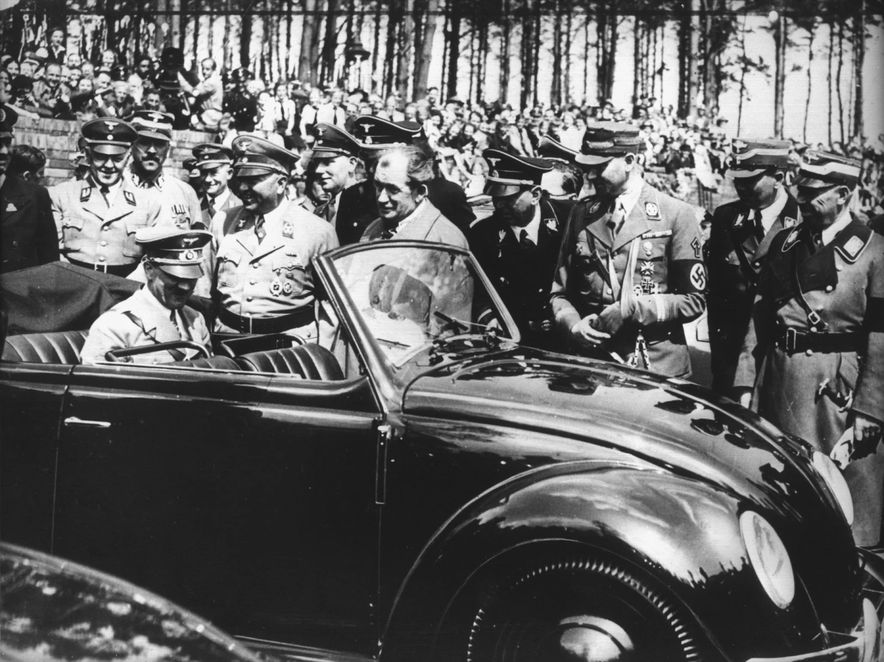 Adolf Hitler begutachtet den ersten Wagen vom Typ Käfer, der 1936 nach den Entwürfen des Automobilkonstrukteurs Ferdinand Porsche (M, ohne Kopfbedeckung) gebaut wurde.