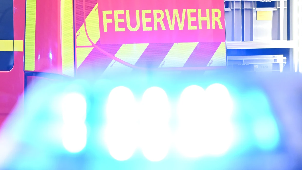 Einsatz: Ein Fahrzeug der Feuerwehr steht bei einem Einsatz auf einer Straße, während im Vordergrund das Blaulicht eines Polizeifahrzeugs zu sehen ist.