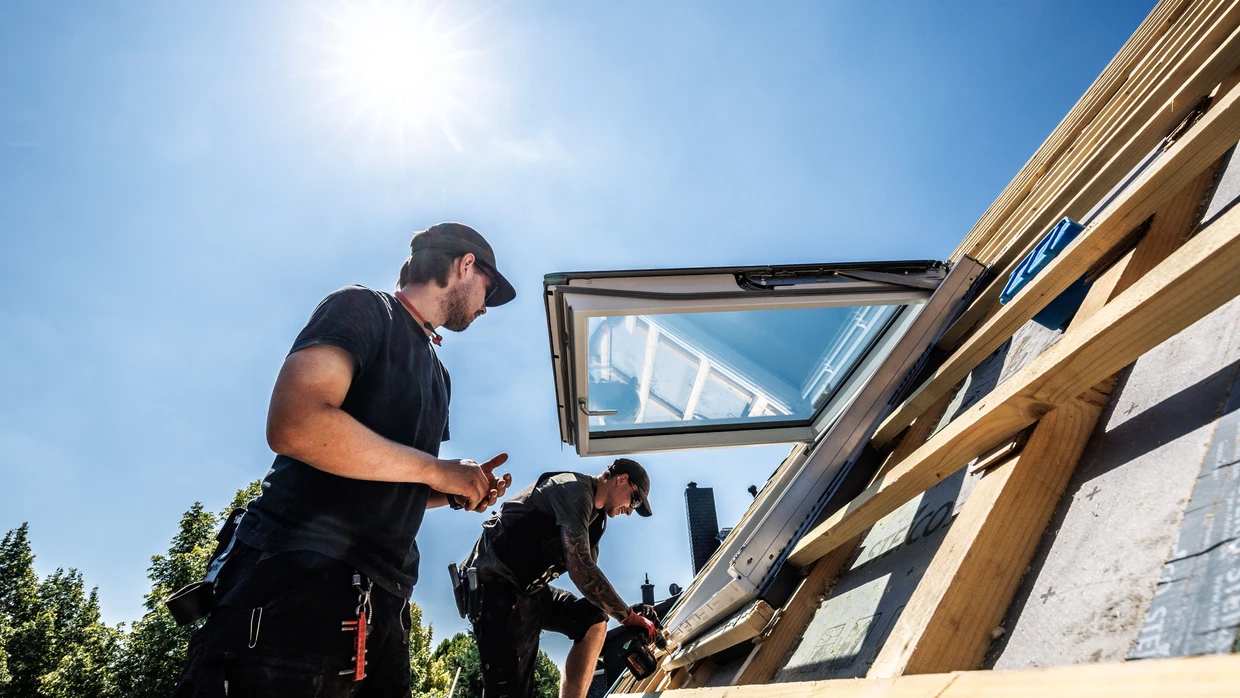 Arbeit bei extremer Hitze: Dachdecker montieren auf einem Dach ein Fenster.