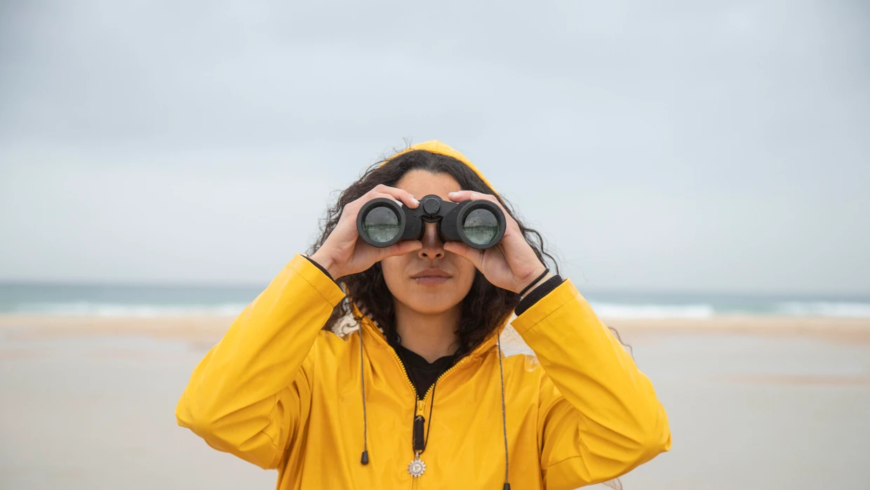 Woman using binoculars while standing at beach