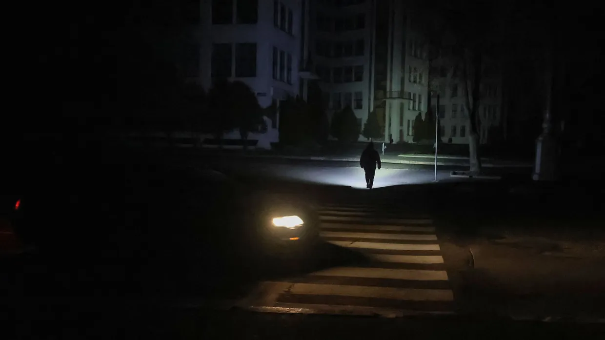 Ein Fußgänger überquert mit einer Taschenlampe einen Zebrastreifen in Charkiw, wo wegen russischer Angriffe der Strom ausgefallen ist, 8.11.25.