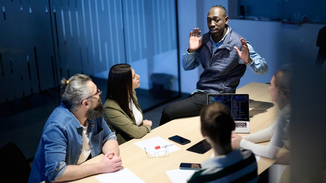 Diverse Business-Team versammelte sich um einen Tisch über Analytik während eines Treffens in einem modernen Büro. Laptop-Bildschirm zeigt Diagramme und Grafiken, symbolisieren Teamwork, Kommunikation und datengesteuerte Strategie