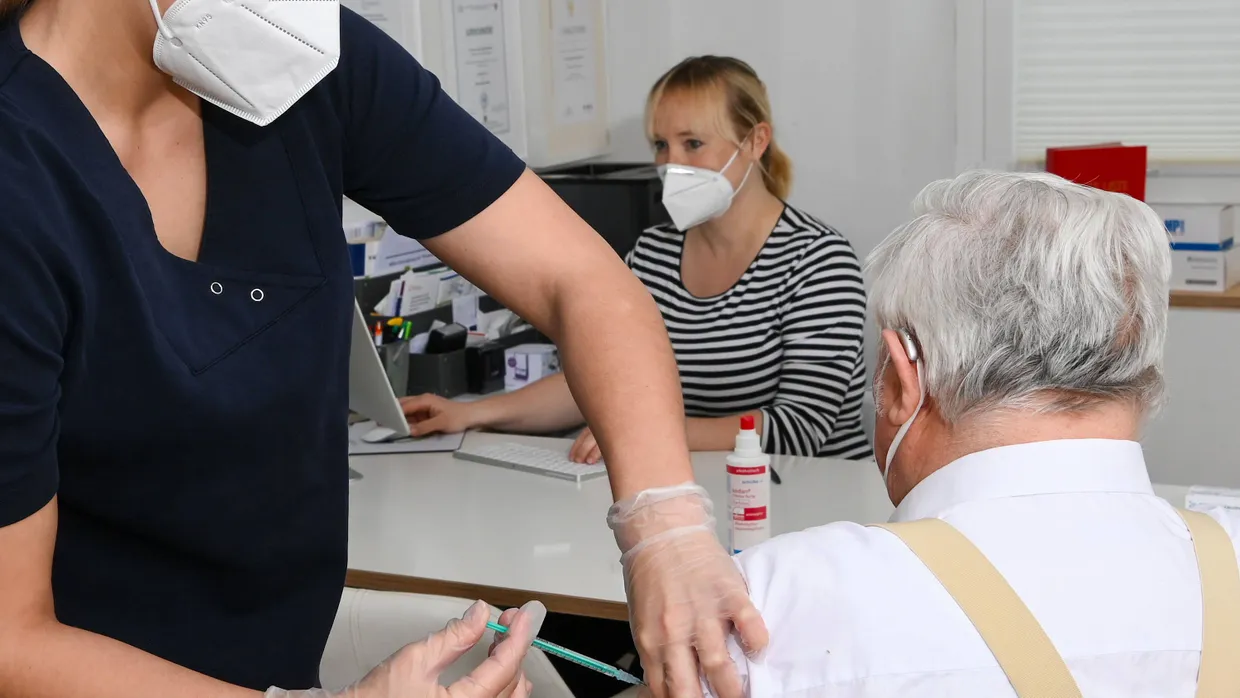 Eine Auszubildende impft einen Patienten in einer Hausarztpraxis.
