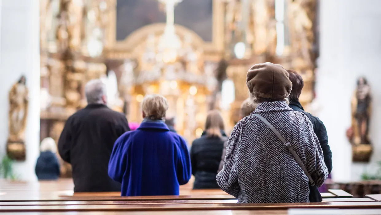 Gottesdienstbesucher stehen während der heiligen Messe in der Karmelitenkirche von Straubing in den Bankreihen.