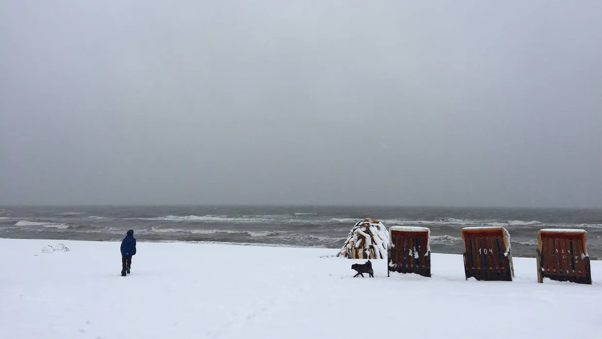 Ein Spaziergänger ist am Ostersonntag mit seinem Hund am verschneiten Strand an der Ostseeküste in Dierhagen (Mecklenburg-Vorpommern) unterwegs.