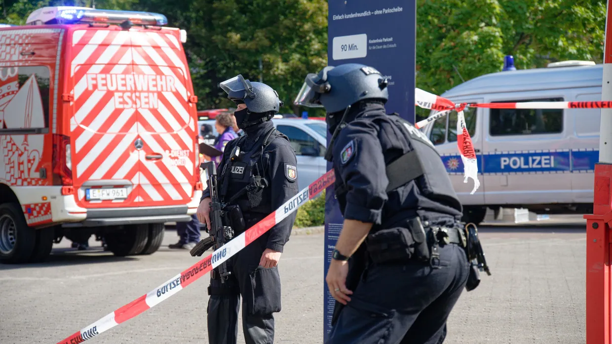 Polizisten stehen an einem Berufskolleg in Essen an einer Absperrung mit Flatterband.