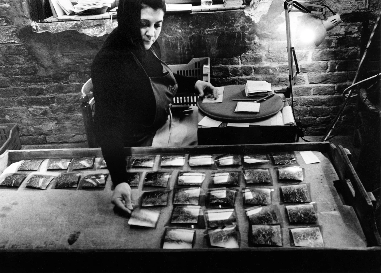 Für die Produktion legt eine Mitarbeiterin Blattgold aus, das mit dem Fragment einer Glasblase belegt wird.