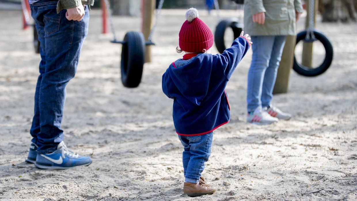 Ein Kind steht mit seinen Eltern auf einem Spielplatz in Berlin.