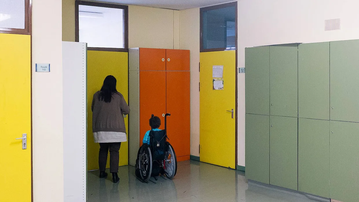 Ein Kind im Rollstuhl wird in seine Klasse gebracht.