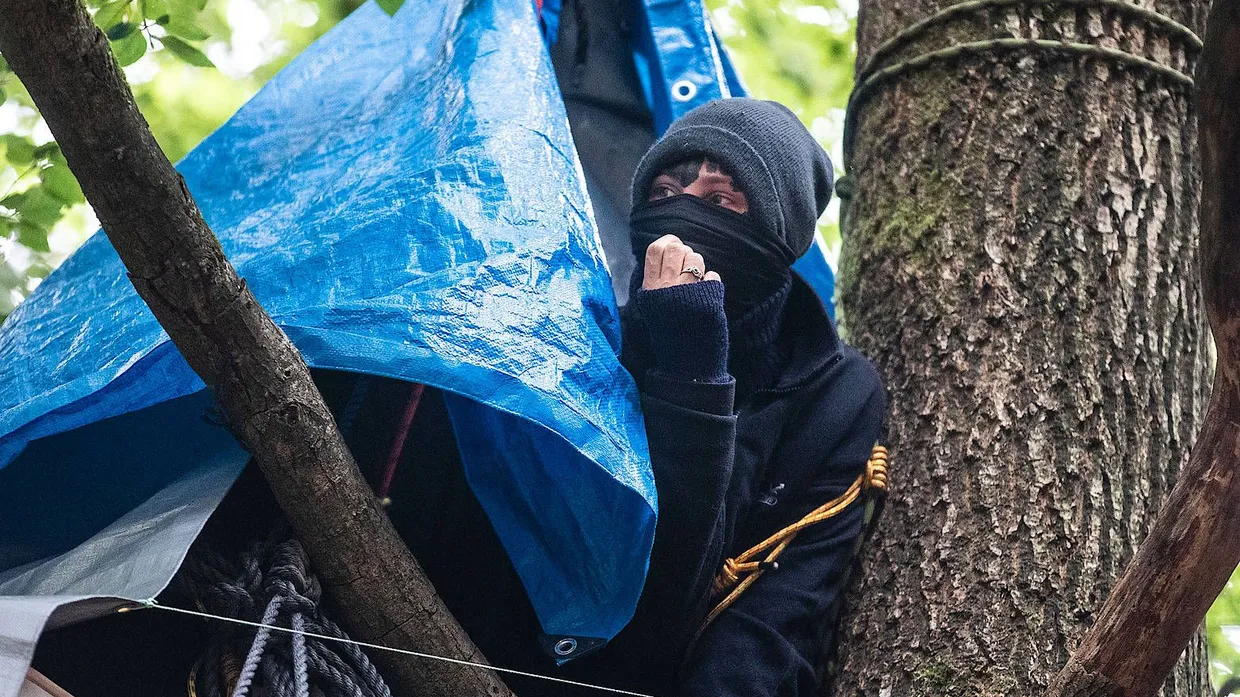Eine vermummte Besetzerin im Herrenwald beobachtet das Geschehen.