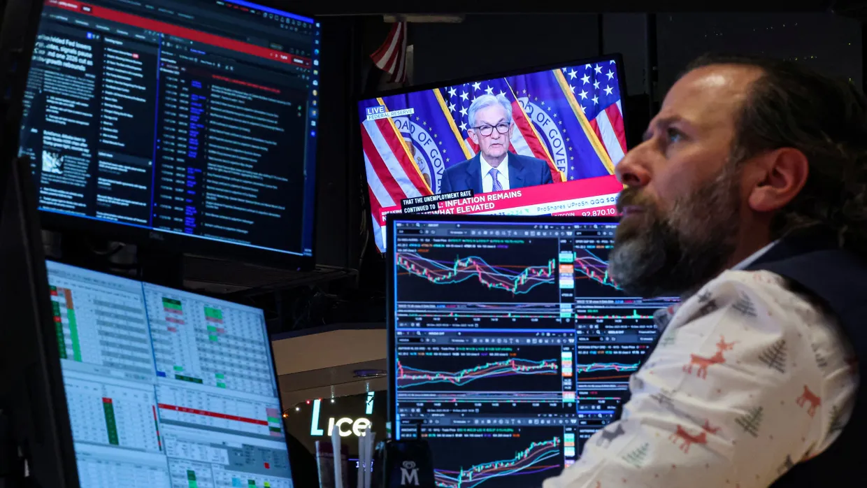 Ein Börsenhändler an der New York Stock Exchange studiert Marktbewegungen, während Fed-Chef Powell die Zinsssenkung erklärt.
