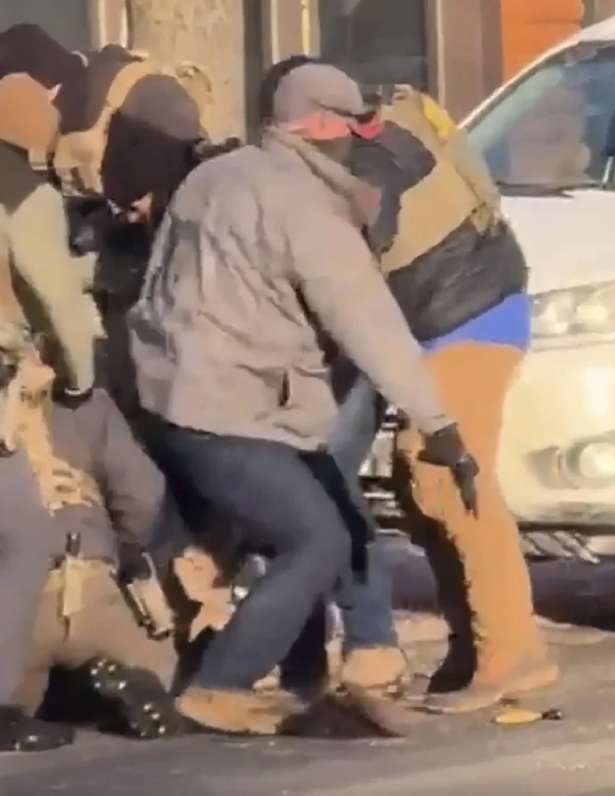 Fotograma del vídeo: un agente federal con una chaqueta gris claro saca un arma de fuego del grupo que rodea a Alex Pretti.