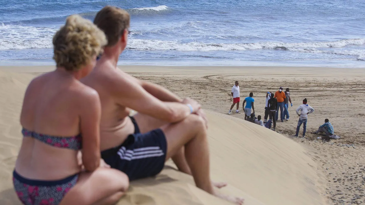Touristen auf der spanischen Insel Gran Canaria beobachten am Strand Migranten