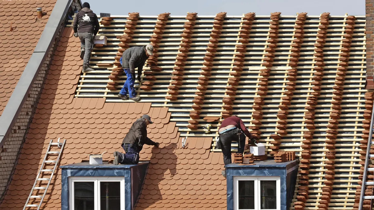 Mit ChatGPT am Bau? Dachdecker decken ein Haus in Bayern mit neuen Ziegeln.