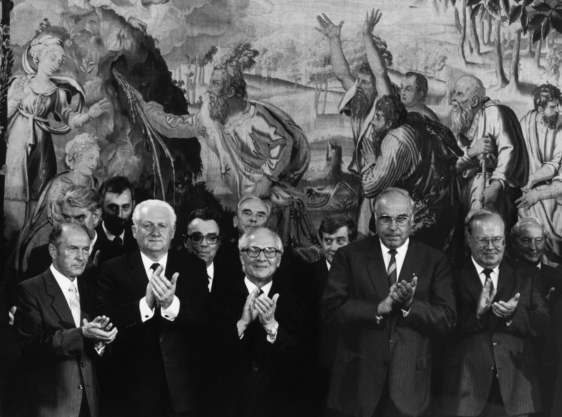Referenz zum Bildhintergrund: Auf dem Gobelin ist der Jubel zu sehen, als Moses Wasser aus dem Fels schlägt. Vorn Staatsbesuch des vergnügten Erich Honecker (Bildmitte) mit dem missgelaunten Helmut Kohl (Zweiter von rechts), Bonn, 1987