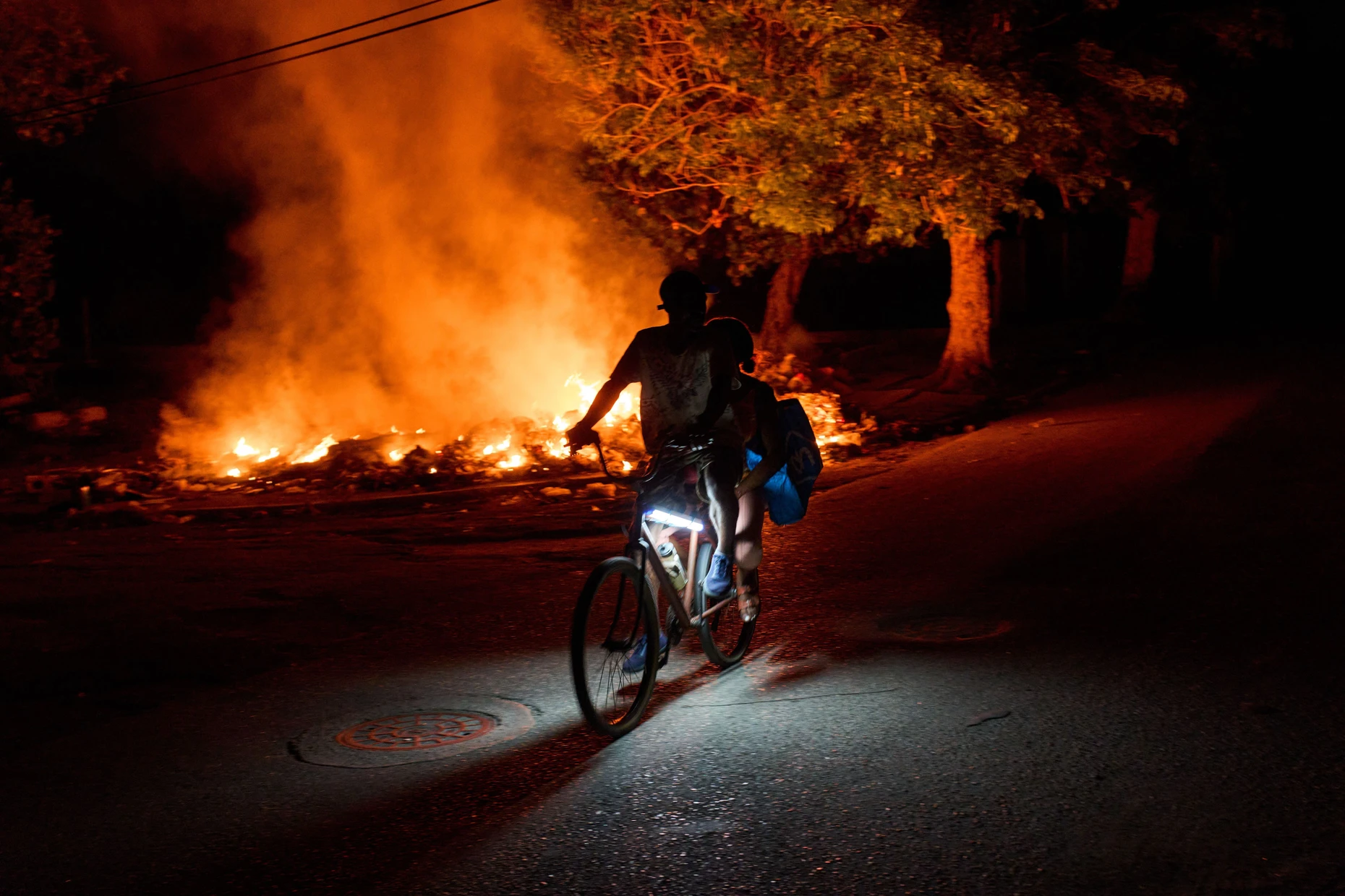 Menschen fahren mit dem Fahrrad an einem Feuer vorbei, das von Anwohnern aus Protest gegen die anhaltenden Stromausfälle auf der Straße gelegt wurde.