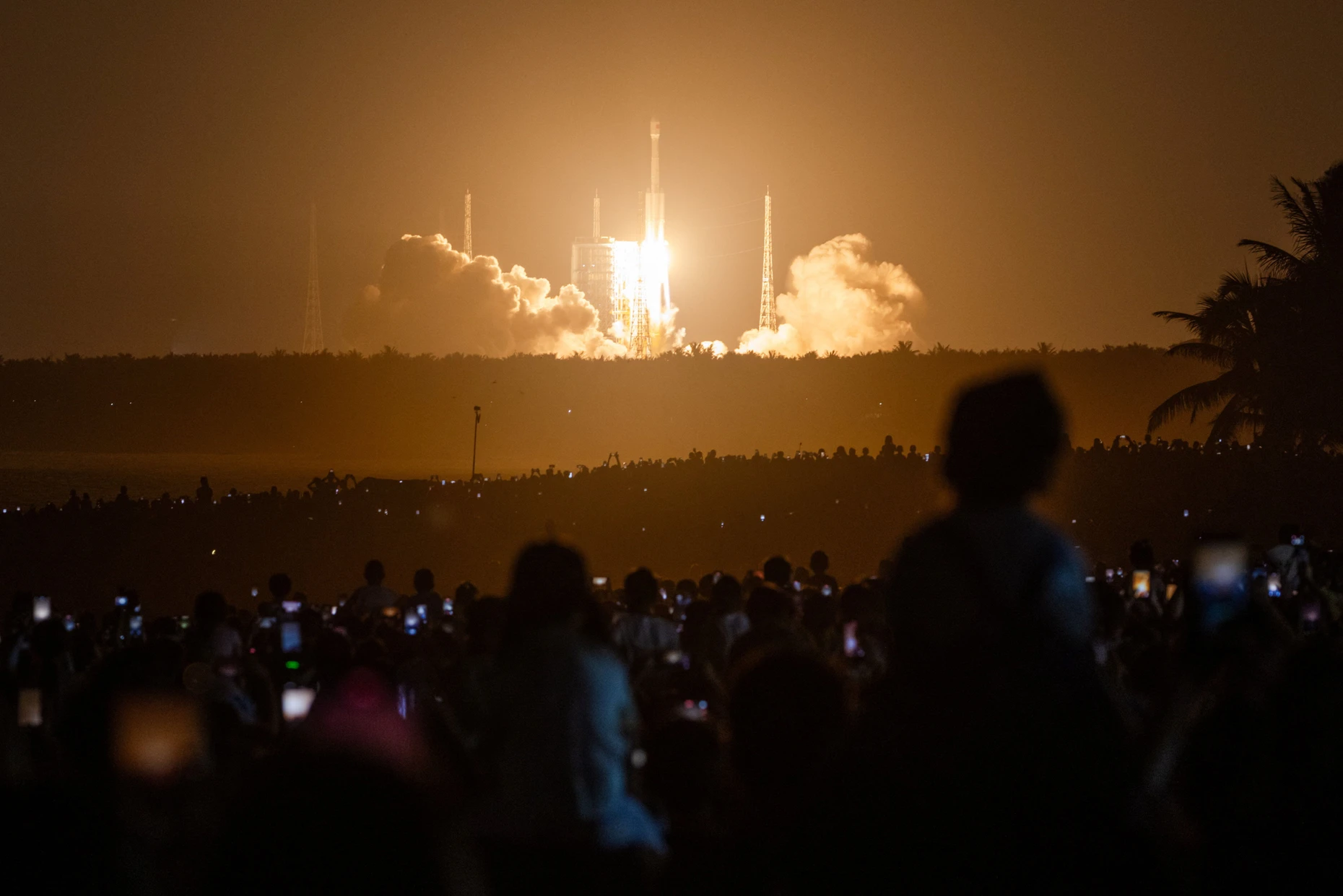 Eine Rakete des Typs Langer Marsch 7A hebt ab, Tausende verfolgen den Start vom Strand aus.