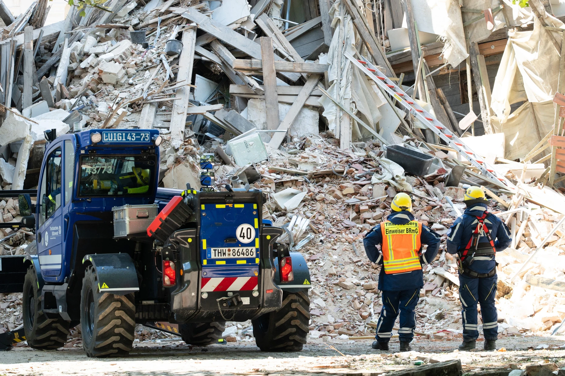 Einsatzkräfte des Technischen Hilfswerks (THW) stehen vor dem Schuttberg des eingestürzten Wohnhauses.