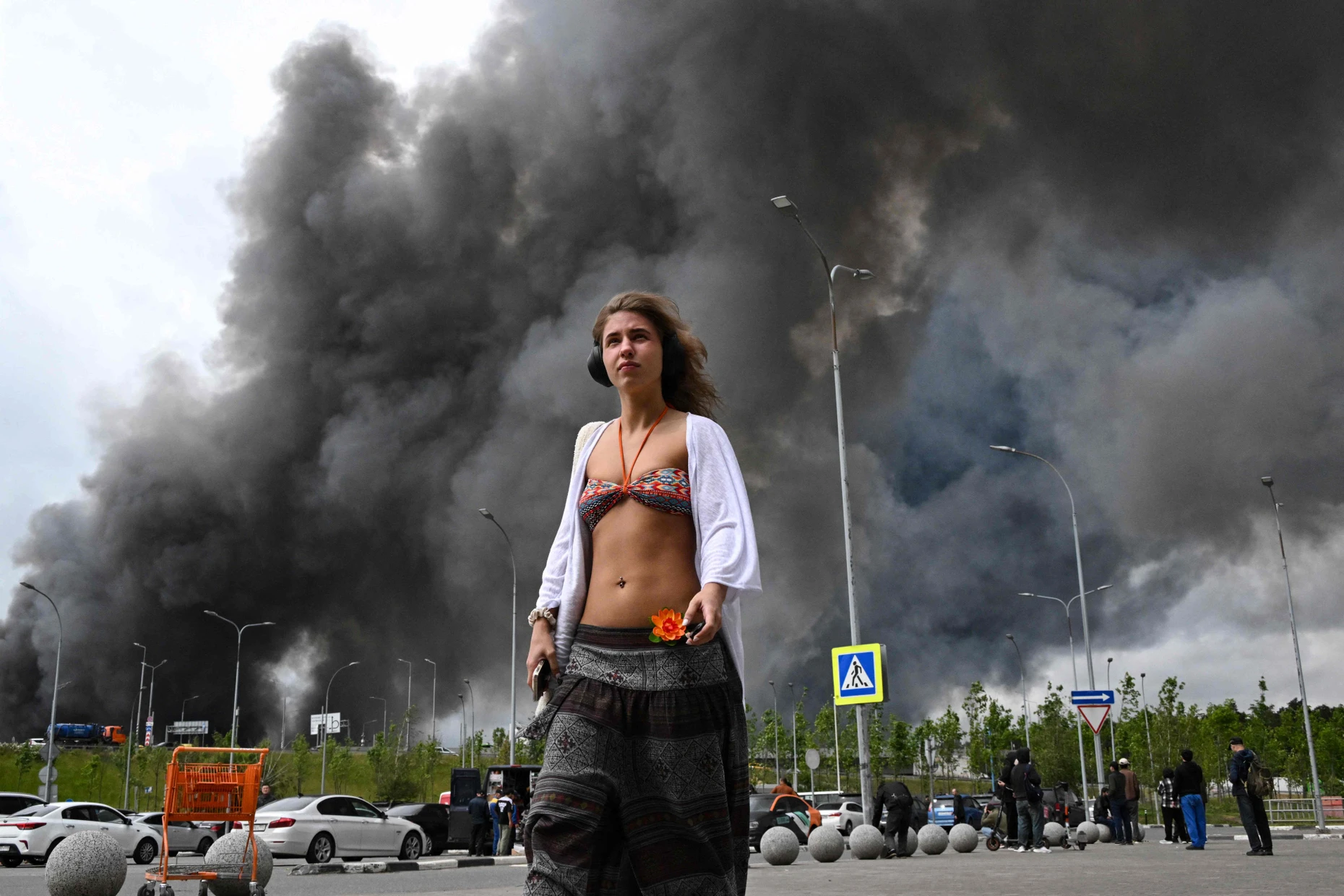 Eine Frau vor einem Moskauer Einkaufszentrum, im Hintergrund brennt die Ölraffinerie von Gazprom.