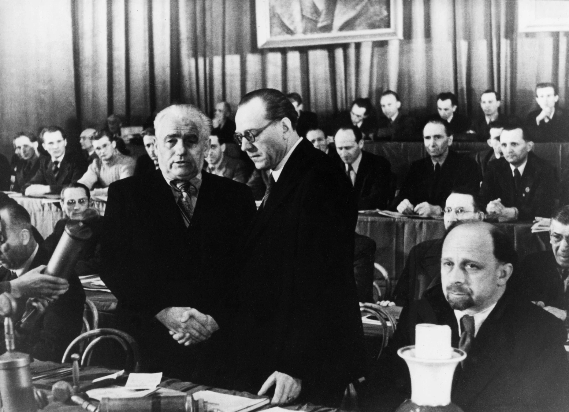 Bei der Gründung der SED durch Vereinigung von SPD und KPD am 21. und 22. April 1946 im Berliner Admiralspalast besiegelten Wilhelm Pieck (links) und Otto Grotewohl, die beiden neugewählten Vorsitzenden der SED, die Zwangsvereinigung mit einem Händedruck. Im Hintergrund zwischen den beiden ist Kurt Müller zu sehen, der danach in Ungnade fiel und wegretuschiert wurde.